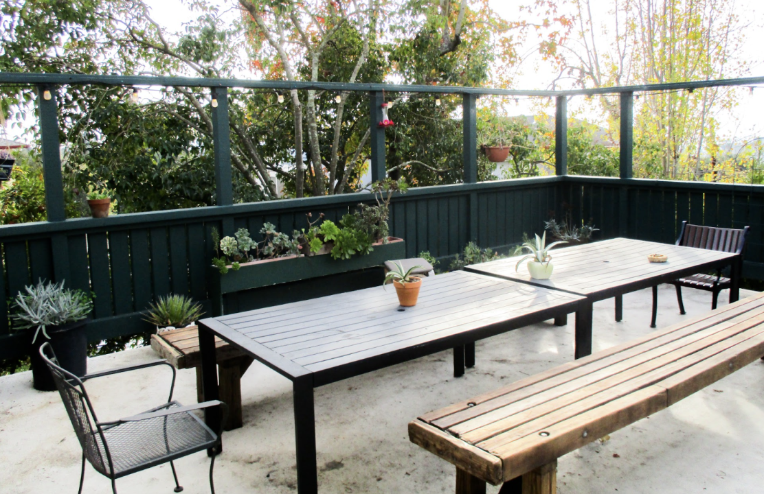 Backyard Patio of a co-op. : A fenced patio area with a simple wooden table, benches, and green trim. Potted succulents and chairs add a cozy, inviting touch.