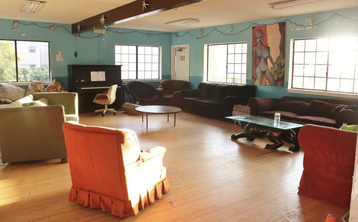 Common area of a co-op. A spacious living room with several couches, large windows, and a colorful mural on the wall, creating an open, communal gathering space.