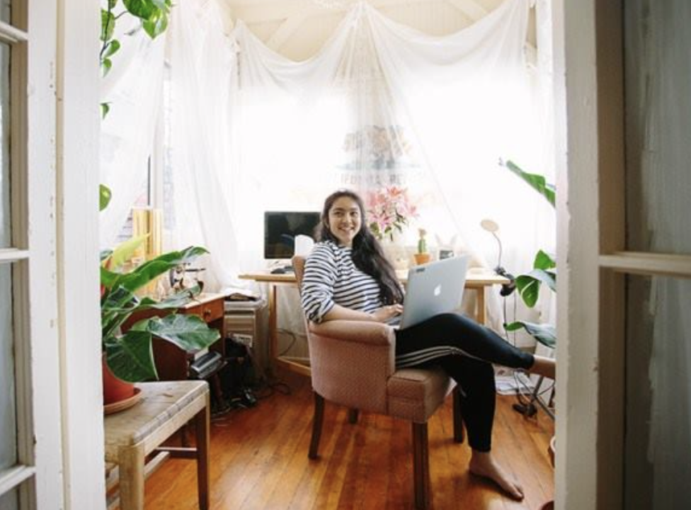 Person studying in room at co-op. A sunlit room filled with houseplants and cozy furniture. A person sits in an armchair, working on a laptop in a serene, natural light.